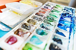 Palette with watercolors in different colors. Various brushes and pencils for drawing prepared by the artist for work.