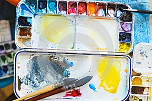 Palette with watercolors in different colors. Various brushes and pencils for drawing prepared by the artist for work.