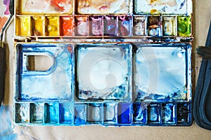 Palette with watercolors in different colors. Various brushes and pencils for drawing prepared by the artist for work.