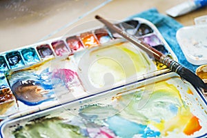 Palette with watercolors in different colors. Various brushes and pencils for drawing prepared by the artist for work.