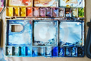 Palette with watercolors in different colors. Various brushes and pencils for drawing prepared by the artist for work.