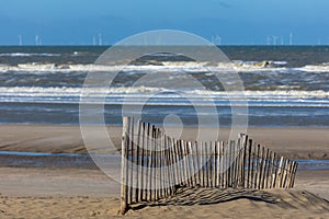 A paling fence on the beach of the North sea in front of a rough sea with spindrift waves