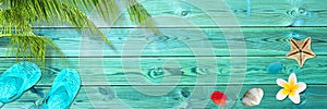 Palm leaf, flip flops and seashells on blue wooden planks, panoramic beach and summer background