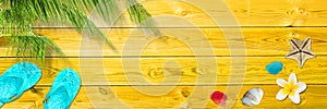 Palm leaf, flip flops and seashells on yellow wooden planks, panoramic beach and summer background