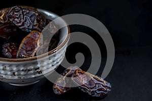 Palm tree fruit dry date on a white bowl on black wooden background, close up