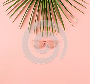 Palm tree leaf and sunglasses on pastel pink background. Minimal summer travel or tropical vacation concept. Copy space