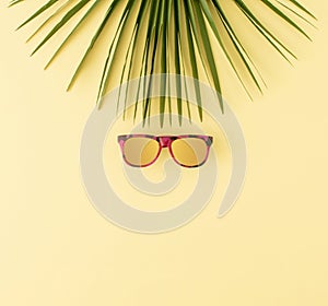 Palm tree leaf and sunglasses on pastel yellow background. Minimal summer travel or tropical vacation concept. Copy space