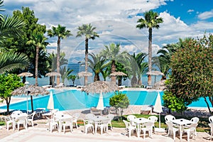Palm trees, beach sunbeds and umbrellas near the pool by the sea in sunny day