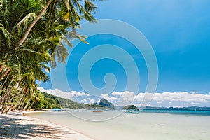 Palm trees of Corong Corong beach with traditional boats and blue sky in El Nido, Palawan island, Philippines