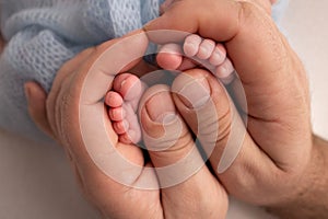 The palms of the father, the mother are holding the foot of the newborn baby
