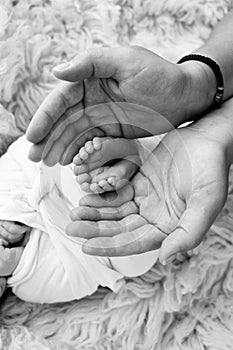 The palms of the father and mother are holding the foot of the newborn baby