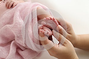 The palms of the father, the mother are holding the foot of the newborn baby in a pink blanket.
