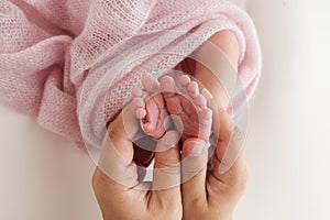 The palms of the father, the mother are holding the foot of the newborn baby in a pink blanket.