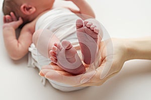 The palms of the father, the mother are holding the foot of the newborn baby in a white blanket.