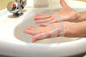 Palms of hands in soapy foam over the sink with a running stream of water. Hand washing