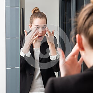 Pampering beautiful young business woman checking her mascara in mirror