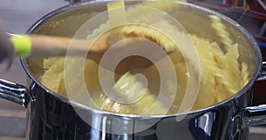 A pan of boiling water and Italian pasta called mafaldine, a woman stirs with a wooden spatula