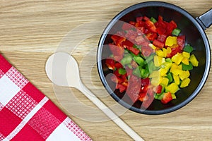 Pan with colorful sliced paprikas on wooden background