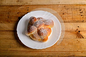 Pan de muerto on a white plate isolated on a wooden table.