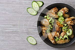 Pan-fried chicken wings and green cucumber on wooden background.