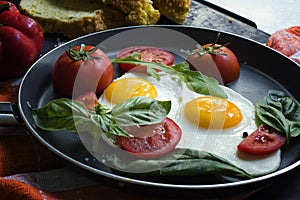 Pan of fried eggs, basil and tomatoes with bread on grunge metallic table surface.