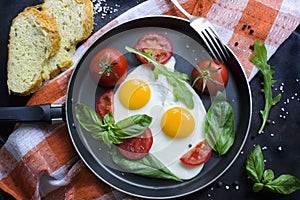 Pan of fried eggs, basil and tomatoes with bread on grunge metallic table surface.