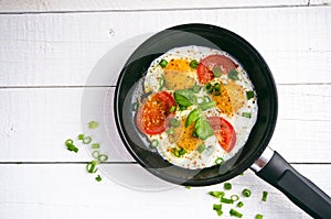 Pan of fried eggs with tomatoes, cheese, spring onion, herbs on a white table. White wooden table. Concept of food. Breakfast time