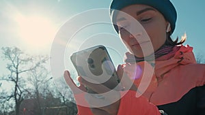 Pan shot caucasian woman in pink choosing music for outdoor workout in winter