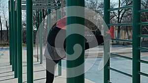 Pan shot caucasian woman stretches outdoors on sports ground bars in winter