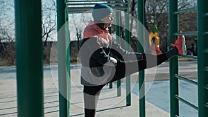 Pan shot caucasian woman stretches outdoors on sports ground bars in winter
