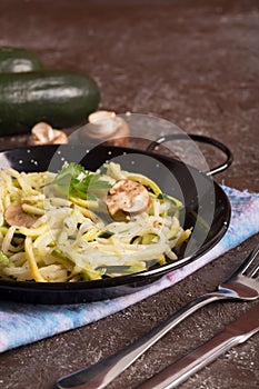 Pan of spaghetti prepared from zucchini and mushroom sauce on wooden table