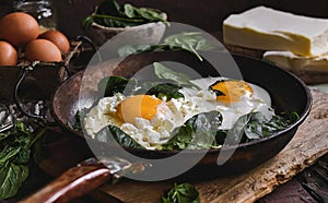 A pan of sunny side up eggs and spinach is on a wooden table with cheese