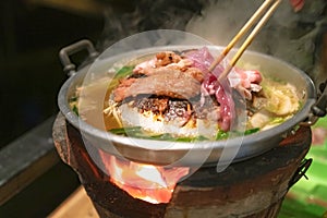 The pan for Thai Barbecue or Moo Kra Ta with raw pork and chopsticks, on top of stove
