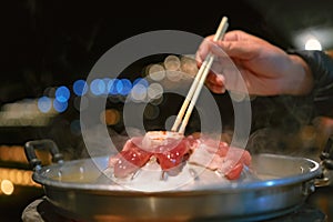 The pan for Thai Barbecue or Moo Kra Ta with raw pork and a hand holding chopsticks