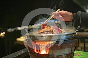 the pan for Thai Barbecue or Moo Kra Ta on top of Thai traditional stove with a woman hand.
