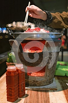 the pan for Thai Barbecue or Moo Kra Ta on top of Thai traditional stove with a woman hand.