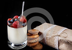 Panakota creamy Italian dessert in a glass cup with berries, next to a stack of ginger cookies and a gift in craft paper in rustic