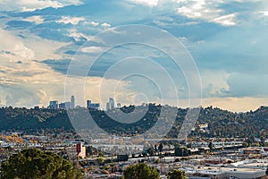 Panaramic view of city businesses and homes with hillside homes and downtown LA towers in the distance