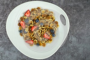 Pancake cereal. Trendy food, mini cereal pancakes in bowl on the table, grey cement background. Trendy baked mini