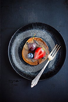 Pancake with fresh berries and chocolate sauce on black plate