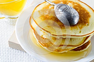 Pancake with honey and silver spoon on a white plate