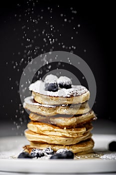 Pancake pile with blueberry sifting powdered sugar on the top of it.