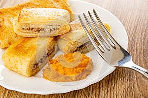 Pancake roll with filling, pieces of pancake, squash caviar in plate, fork on wooden table