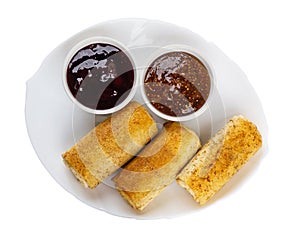 Pancake rolls, bowls with jams in plate isolated on white background. Top view