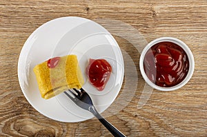 Pancake rolls with meat on fork, ketchup in saucer, bowl with tomato sauce on wooden table. Top view