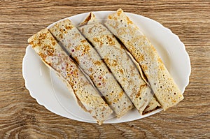 Pancake rolls in white plate on wooden table. Top view