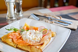 Pancake with salmon and sourcream and dille on a white plate.