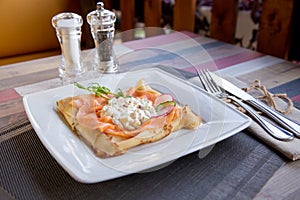 Pancake with salmon and sourcream and dille on a white plate.