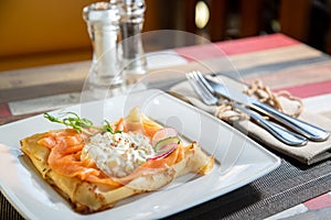 Pancake with salmon and sourcream and dille on a white plate.