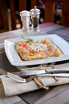 Pancake with salmon and sourcream and dille on a white plate.